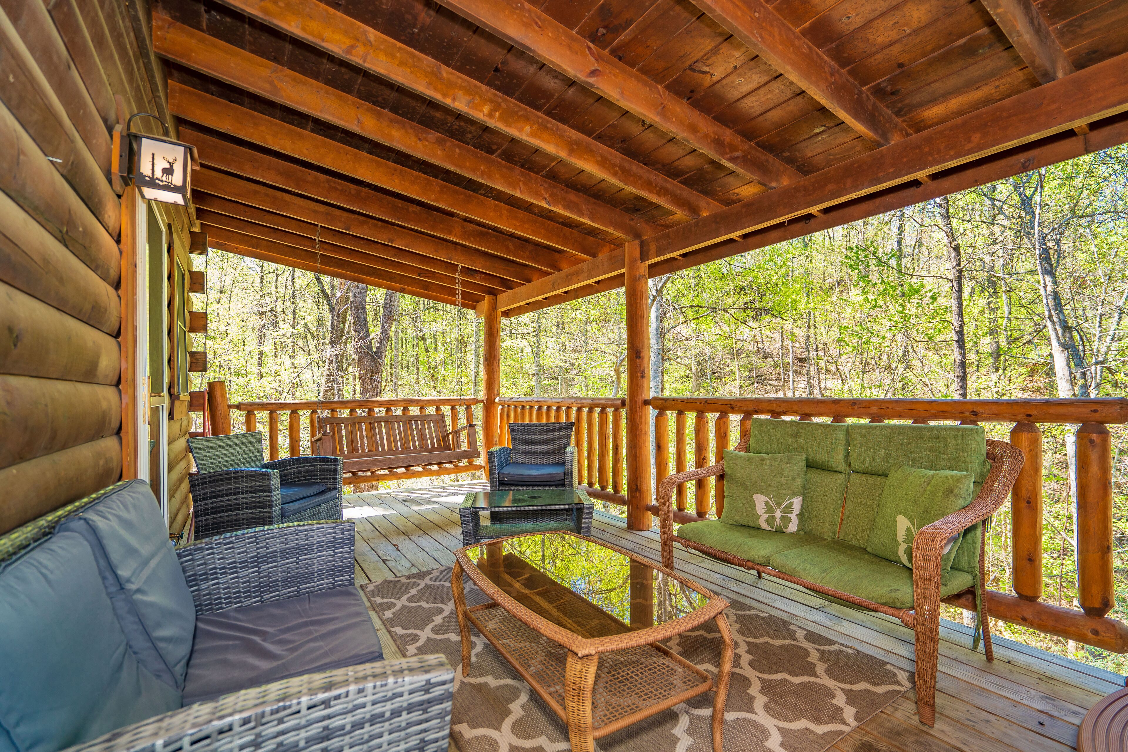 A covered porch with wicker furniture, a glass-top table, and a view of a forest.