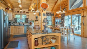 A wooden cabin interior with a kitchen, dining area, and large windows. - 🌲Night Moves Over The Smokies 🌙 Hot Tub, Pool Table & Porch Swing (Sevierville)
