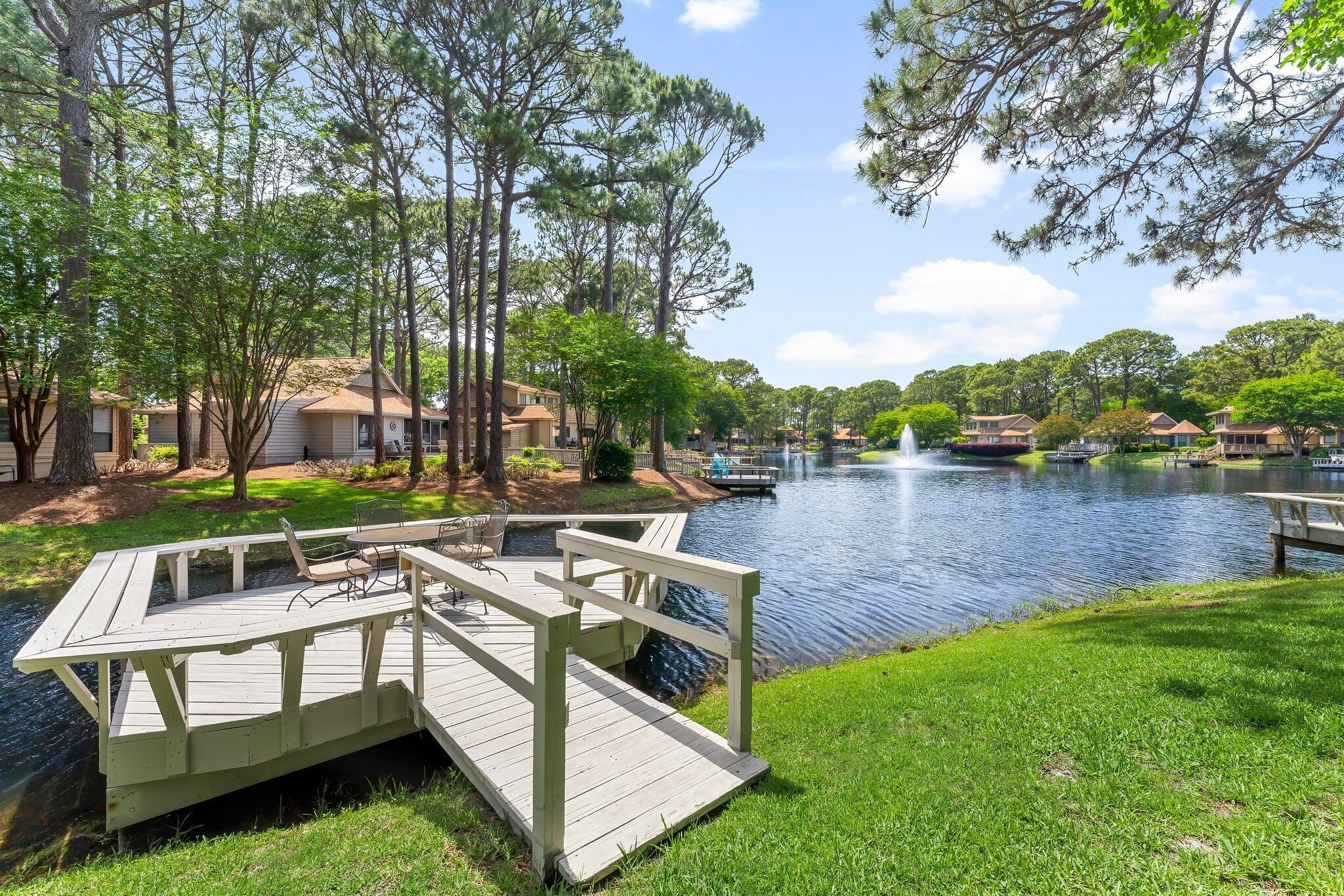 A lakeside deck with a fountain, surrounded by trees and houses.