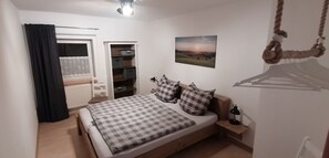 Une chambre à coucher comprenant un lit, une armoire, un radiateur, une fenêtre avec des rideaux, un luminaire suspendu et un tableau accroché au mur.