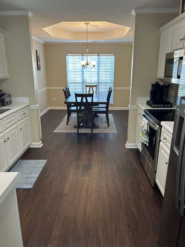 A kitchen with a dining table, chairs, cabinets, a refrigerator, and a coffee maker.
