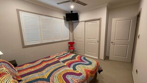 Une chambre à coucher avec un lit, une télévision, une fenêtre avec des stores et deux portes.