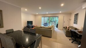 Una sala de estar moderna con una mesa de comedor, sofás, un televisor y un balcón con vistas.