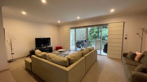 Un salon moderne avec un canapé, un téléviseur et un balcon équipé d’une table et de chaises.