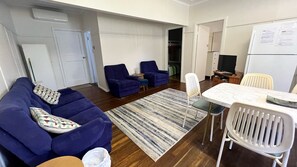 A living room with a sofa, two armchairs, a coffee table, and a dining table with chairs. - Cabenay Unit 2 - Close to Beach (South West Rocks)