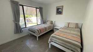 A bedroom with two beds, a window with curtains, a small table, and a framed picture on the wall.