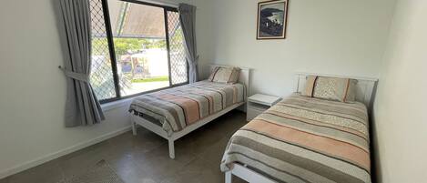 A bedroom with two beds, a window with curtains, a small table, and a framed picture on the wall.