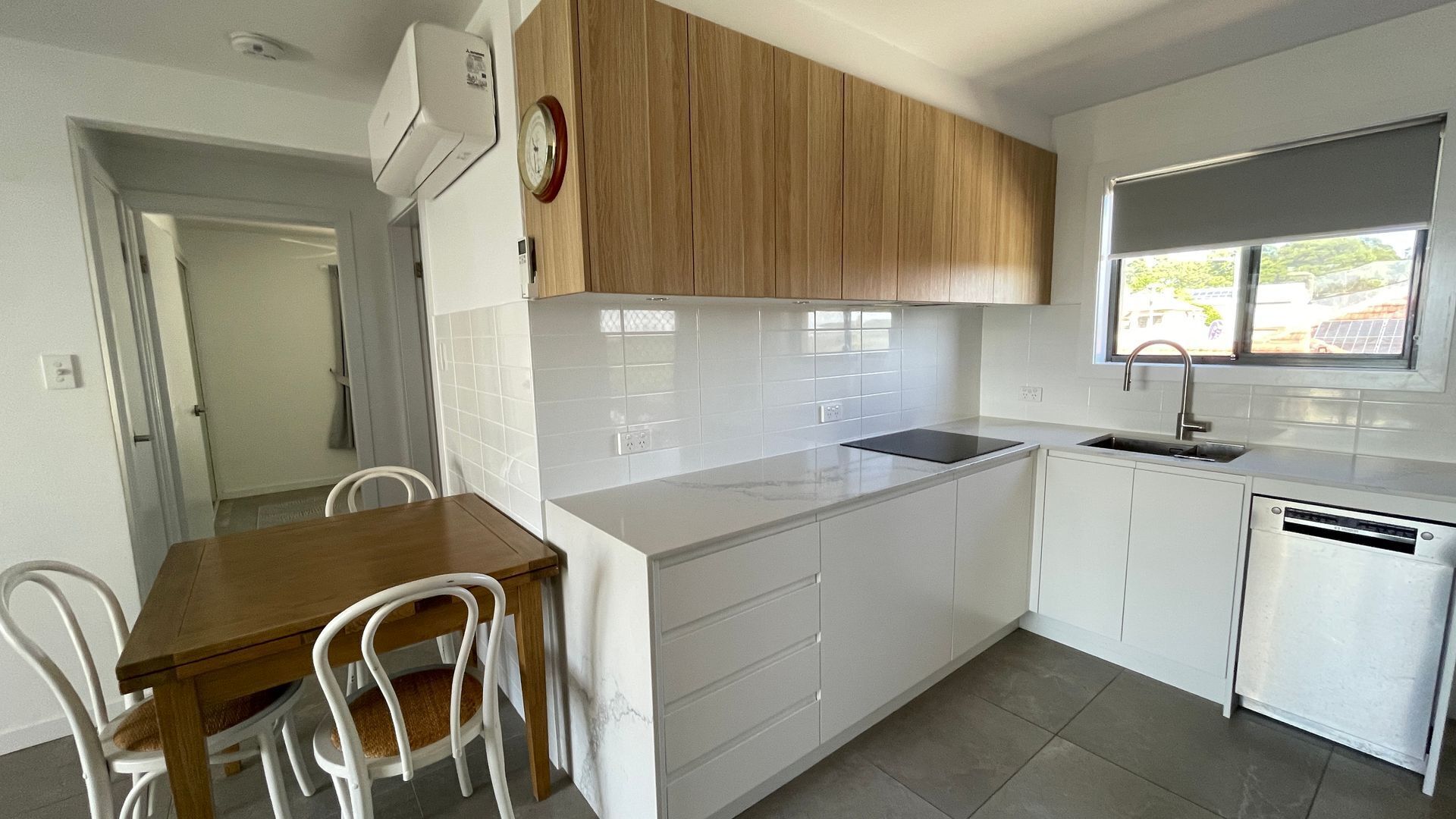 A compact kitchen with white cabinets, a wooden dining table, and a built-in dishwasher.