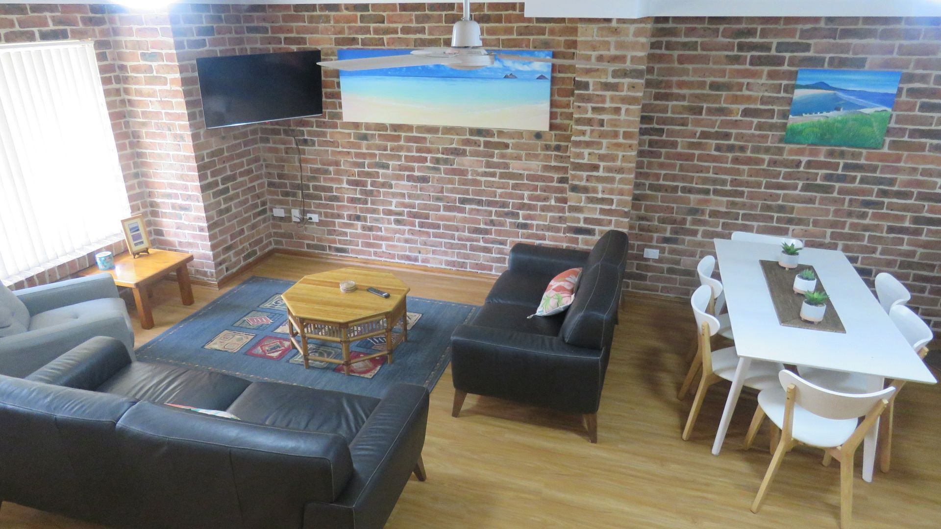Ein Wohnzimmer mit Backsteinwand, einem Flachbildfernseher, einer Couch, einem Couchtisch und einem Essbereich mit Tisch und Stühlen.