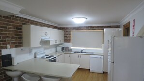 A compact kitchen with white cabinets, a stove, a microwave, and a refrigerator. - BIRCHGROVE 3 - 400 METRES TO BEACH (SOUTH WEST ROCKS)