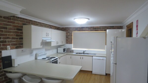 A compact kitchen with white cabinets, a stove, a microwave, and a refrigerator.