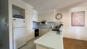 A modern kitchen with white cabinetry, a built-in microwave, a clock on the wall, and a welcome sign on the refrigerator. - TRADEWINDS UNIT 7 - BEACH VIEWS (South West Rocks)