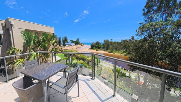 Uma varanda com mesa e cadeiras, com vista para uma praia e um rio.