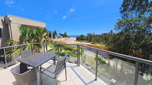 Un balcón con mesa y sillas, con vista a una playa y un río.
