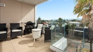 A balcony with wicker furniture, a grill, and a glass enclosure overlooking a residential area. - Awesome Downtown Location - Park & Walk (Tauranga)