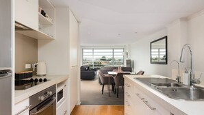 A modern kitchen with white cabinetry, a stainless steel sink, and a dining area with a gray sofa and table. - Awesome Downtown Location - Park & Walk (Tauranga)