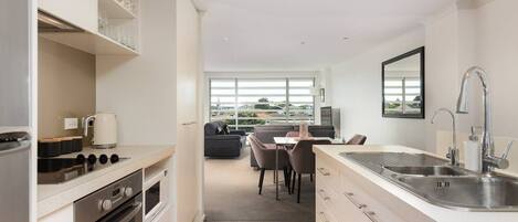 A modern kitchen with white cabinetry, a stainless steel sink, and a dining area with a gray sofa and table.