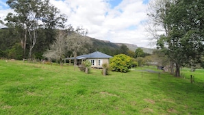 A house with a fenced yard, surrounded by trees and hills in the background.