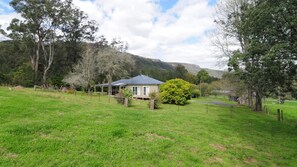 Situated on a lush green lawn, this single-story house offers a serene rural retreat amidst a natural mountainous landscape.