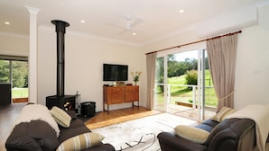 A living room with a fireplace, a sofa set, a television, and a view of a garden through large sliding doors.