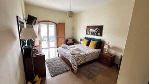 A bedroom with a bed, bedside tables, a desk, a chair, a lamp, a painting, and a view through a door. - "Luz House" charming apartment with Jacuzzi (Luz (Luz de Tavira))