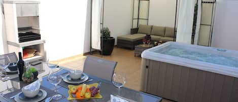 A dining area with a table set for two, a hot tub, and a covered seating area.