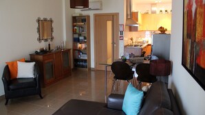 A living room with a sofa, a dining table with chairs, a bookshelf, and a kitchen area in the background. - "Luz House" charming apartment with Jacuzzi (Luz (Luz de Tavira))
