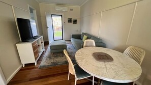 A compact living space with a television, sofa, and dining table. - CABENAY UNIT 1 - GROUND FLOOR PARK VIEWS (SOUTH WEST ROCKS)