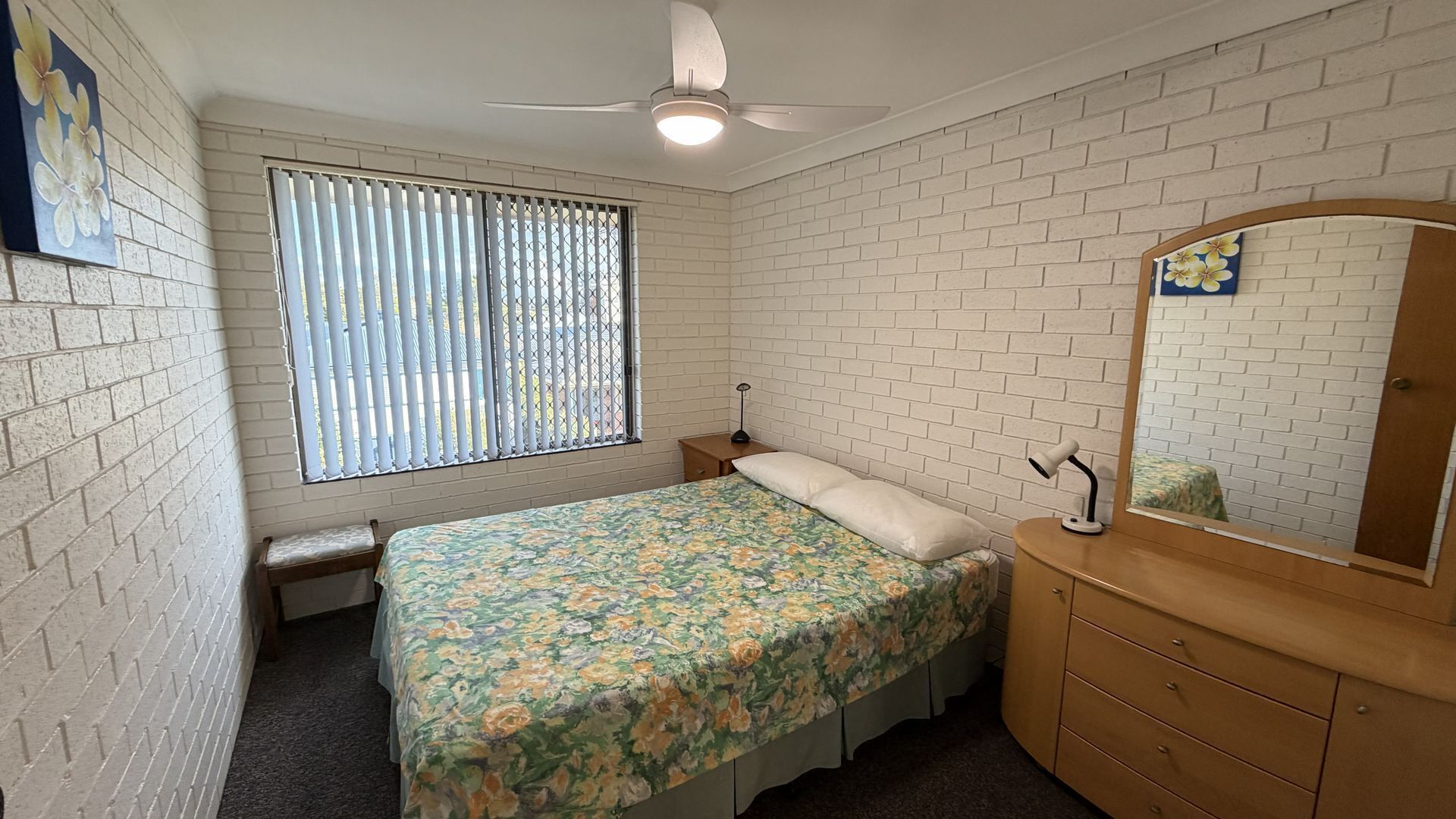 A bedroom with a bed, a dresser, a mirror, a ceiling fan, and a window with blinds.