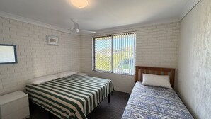 A room with two beds, a ceiling fan, a window with bars, and a picture frame on the wall. - WOODY WONDER UNIT 8 - TOP FLOOR GREAT LOCATION (SOUTH WEST ROCKS)