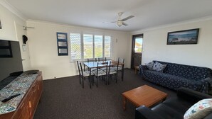 A living room with a sofa, a coffee table, a dining table with chairs, a ceiling fan, and a window with blinds. - WOODY WONDER UNIT 8 - TOP FLOOR GREAT LOCATION (SOUTH WEST ROCKS)