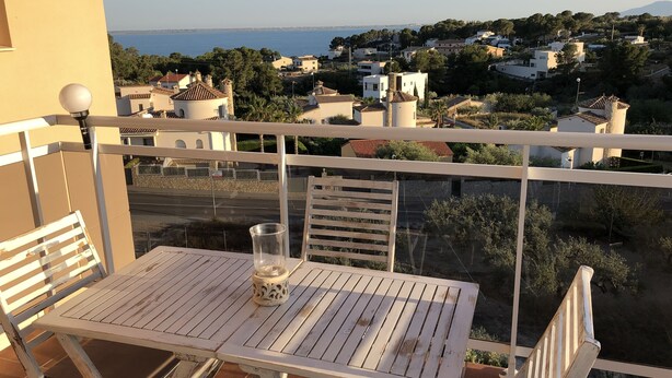 En balkon med bord og stole, der kigger ud over en kystby med bygninger og havudsigt.