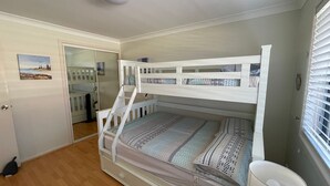 Un lit superposé avec une literie à motifs, une porte blanche et une petite fenêtre avec des stores.