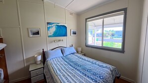 A bedroom with a bed, bedside tables, a window with a view, and a wave painting on the wall. - MITILENE - PARK VIEWS (South West Rocks)