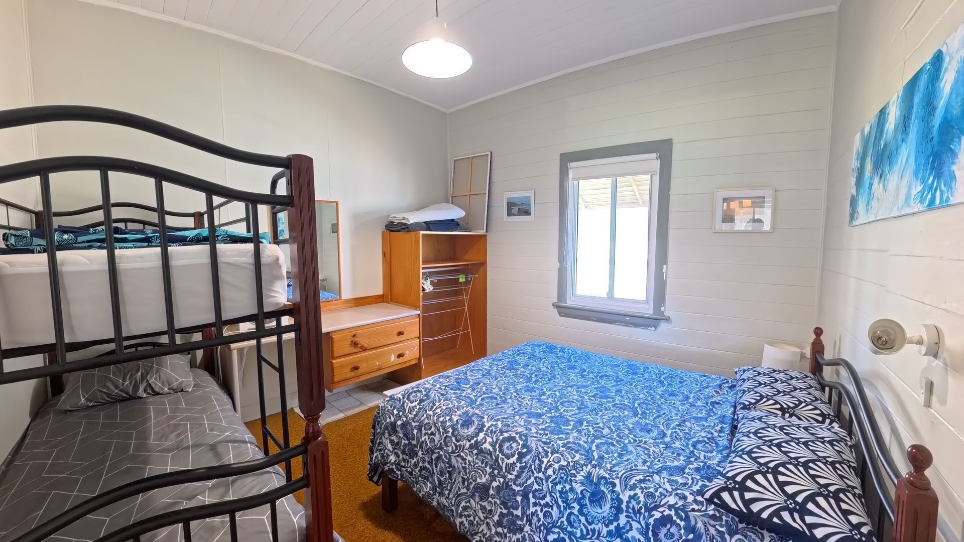A room with bunk beds, a wooden dresser, a window, and a painting on the wall.