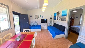 A compact room with a dining table, two sofas, a TV, and a bookshelf. - MITILENE - PARK VIEWS (South West Rocks)