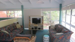 Una sala de estar con dos sofás estampados, un televisor sobre un mueble de madera y un ventilador cerca de la ventana.