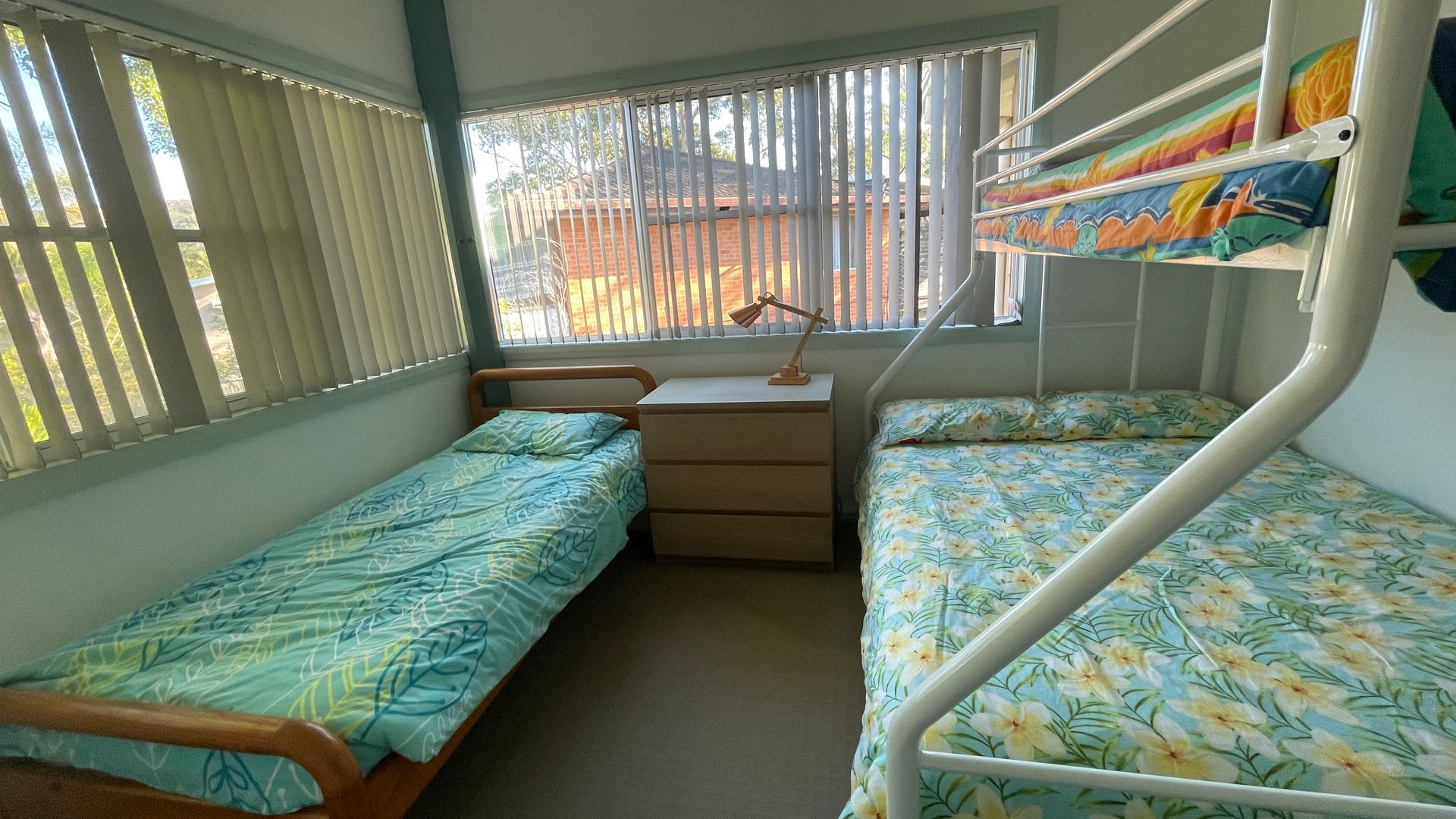 Ein Zimmer mit zwei Etagenbetten, einem Schreibtisch mit Lampe und einem Fenster mit Jalousien.