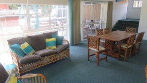 Una habitación con sofá, sillas de madera, una mesa y vistas a través de un ventanal.