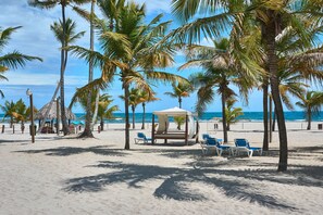 A beach with palm trees, a gazebo, and beach chairs.