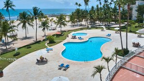 A resort with a large pool, palm trees, and a beach view. - Trendy Beach Scene at a Harmony Beachfront Condo in Costa del Sol (Playa Juan Dolio)