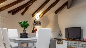 A dining area with a table, chairs, a potted plant, a television, and a stone wall.
