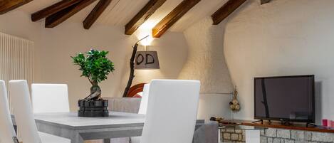 Un comedor con una mesa, sillas, una planta en maceta, un televisor y una pared de piedra.