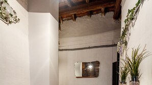 A room with a white sofa, a rug, a white console table with plants, and a wooden ceiling.