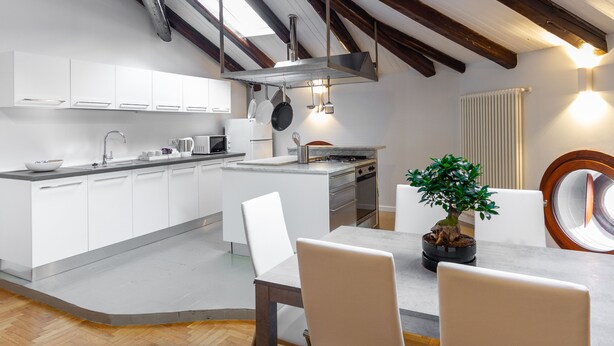 A modern kitchen with white cabinets, a central island, and a dining area with a table and chairs.