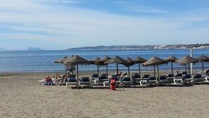 A beach with rows of sun loungers and thatched umbrellas, a clear sky, and a calm sea. - Ideal and front line beach location (Estepona)