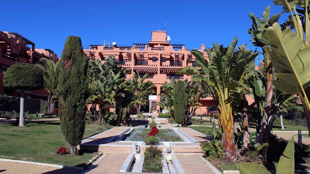 A hotel with a central courtyard, surrounded by lush greenery and palm trees. - Ideal and front line beach location (Estepona)
