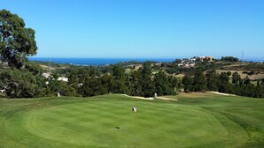 A golf course with a flagstick in the center, surrounded by lush greenery and a clear view of the ocean in the background. - Ideal and front line beach location (Estepona)