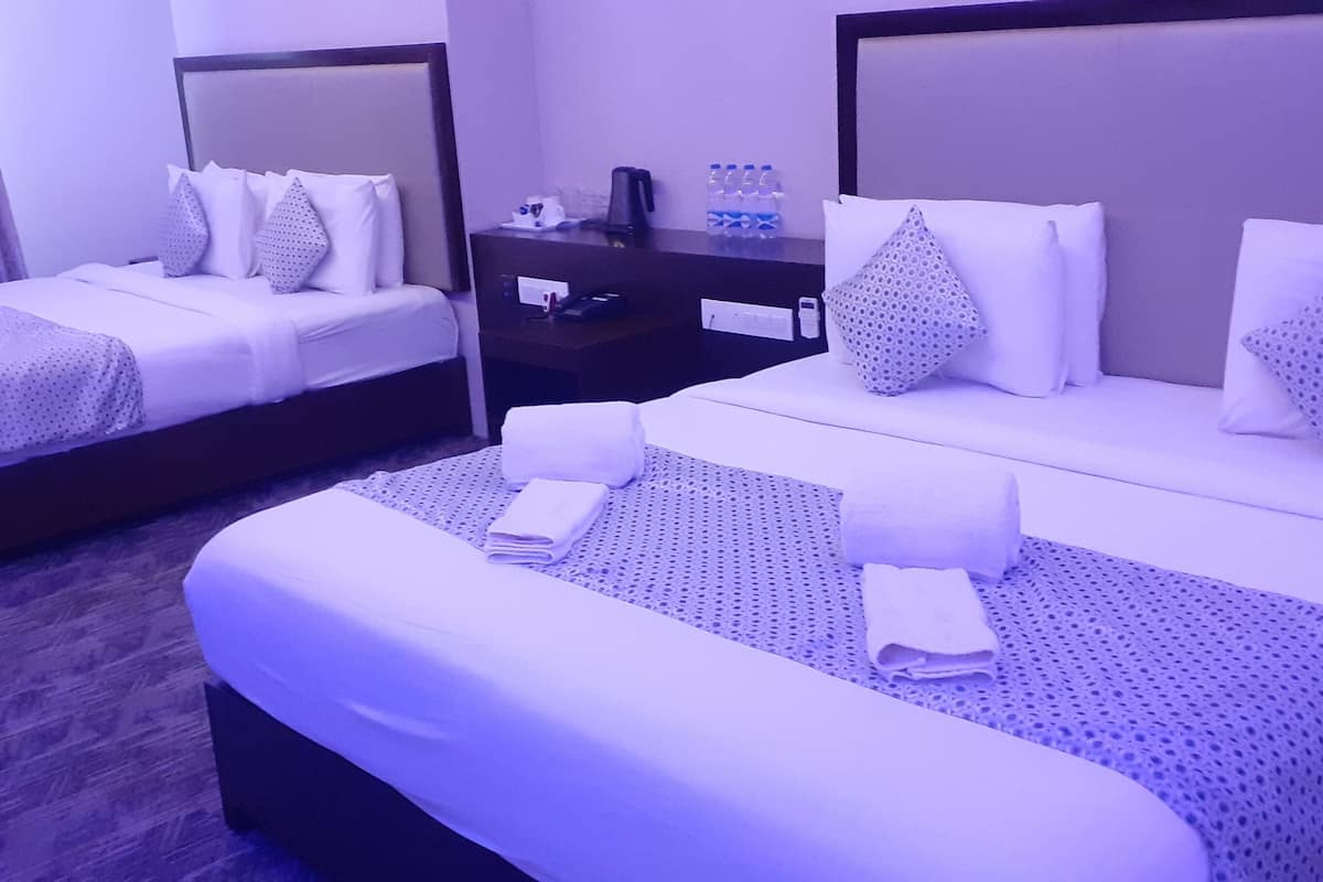 Ein Hotelzimmer mit zwei Betten, jeweils mit weißer Bettwäsche und gemusterten Kissen. Ein Nachttisch mit Kaffeemaschine und Wasserflaschen steht bereit.