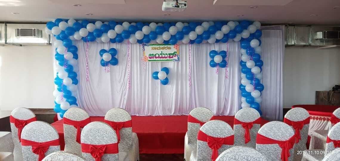 A stage with blue and white balloons, a red tablecloth, and white chairs with red sashes.